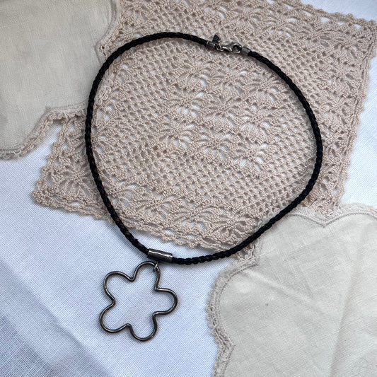Black necklace with a floral pendant on a textured fabric background